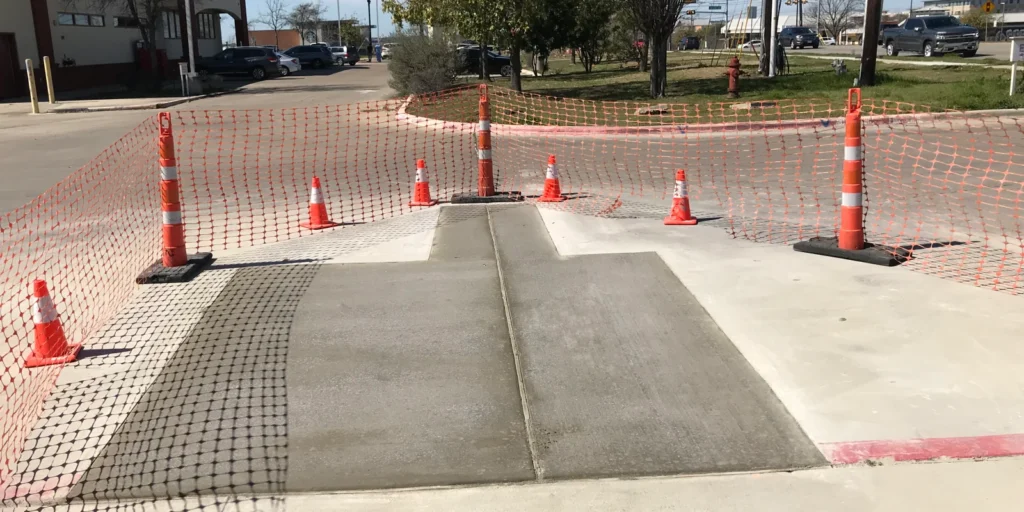 Freshly poured concrete ramp, expertly crafted to prevent future wear and tear, is sectioned off with orange safety cones and netting. The careful attention to detail ensures that concrete crack filling won't be necessary anytime soon.
