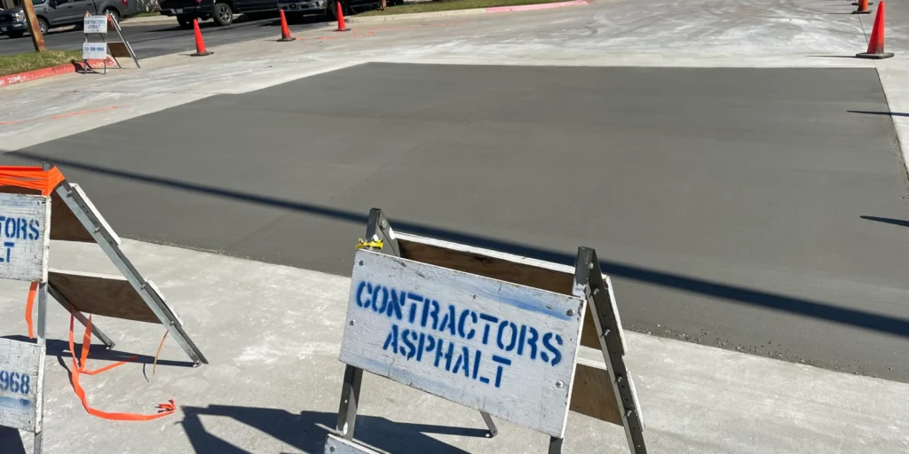 A freshly paved asphalt section features traffic cones and two contractor signs in the foreground, hinting at recent concrete pothole repairs that promise a smoother drive.